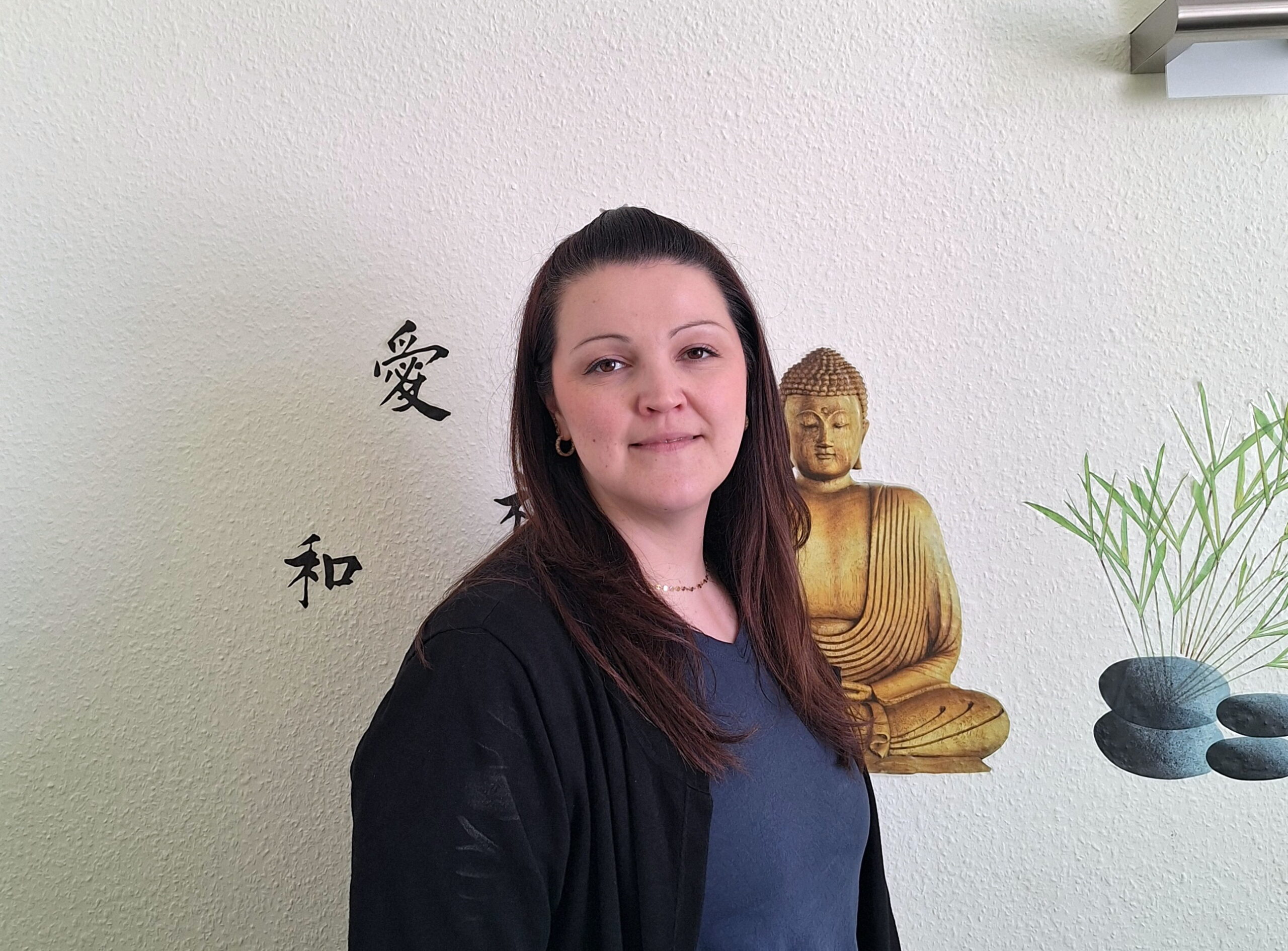 Mitarbeiterin-Julia-Bohla Mitarbeiterin Julia Bohla vor Wand mit goldener Buddha-Figur und Bambus-Dekor im MIWE Gesundheitszentrum