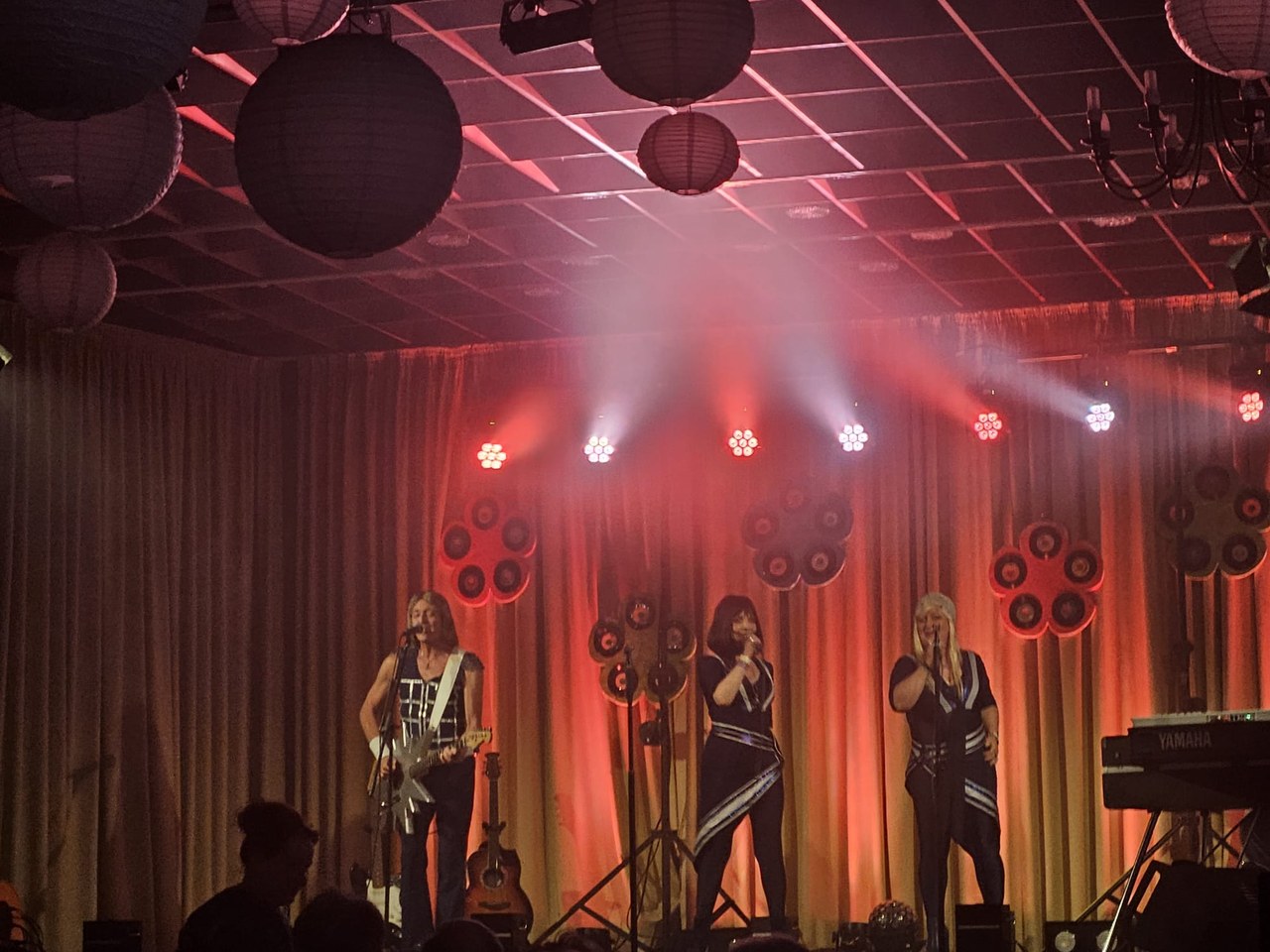 Drei Mitglieder der ABBA Revival Show „A4u“ in den ikonischen blau-weißen ABBA-Kostümen im warmen Bühnenlicht
